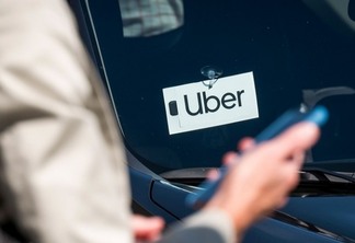 A traveler uses a smartphone in front of a vehicle displaying Uber Technologies Inc. signage at the Oakland International Airport.